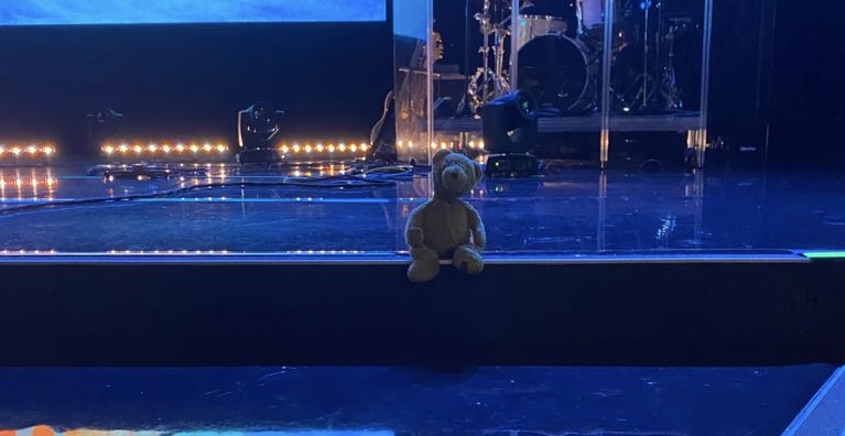 A photo of a teddy bear sitting on a stage staring at the camera
